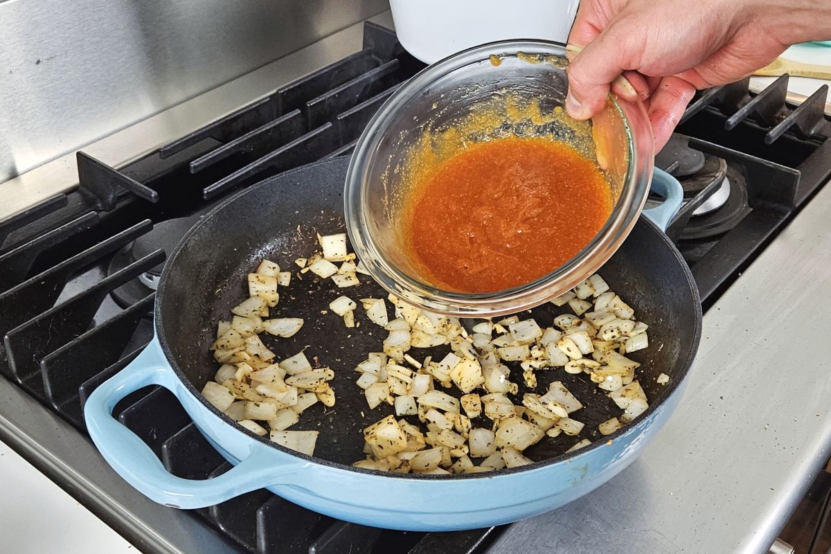 Someone pouring  apricot sauce in a pan with cooked onions and garlic. 