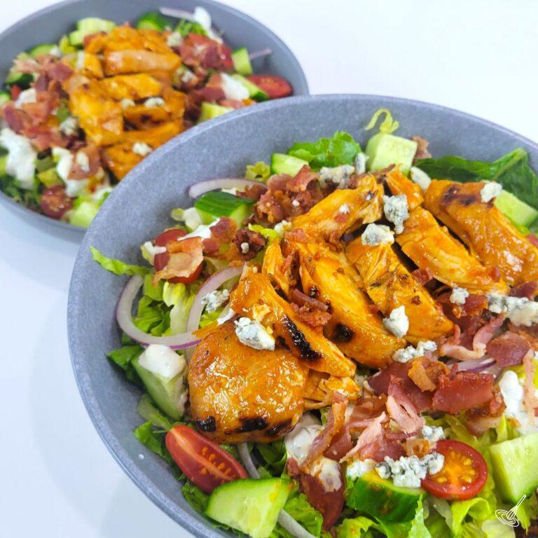Grilled chicken on top of a bed of lettuce, on a plate.