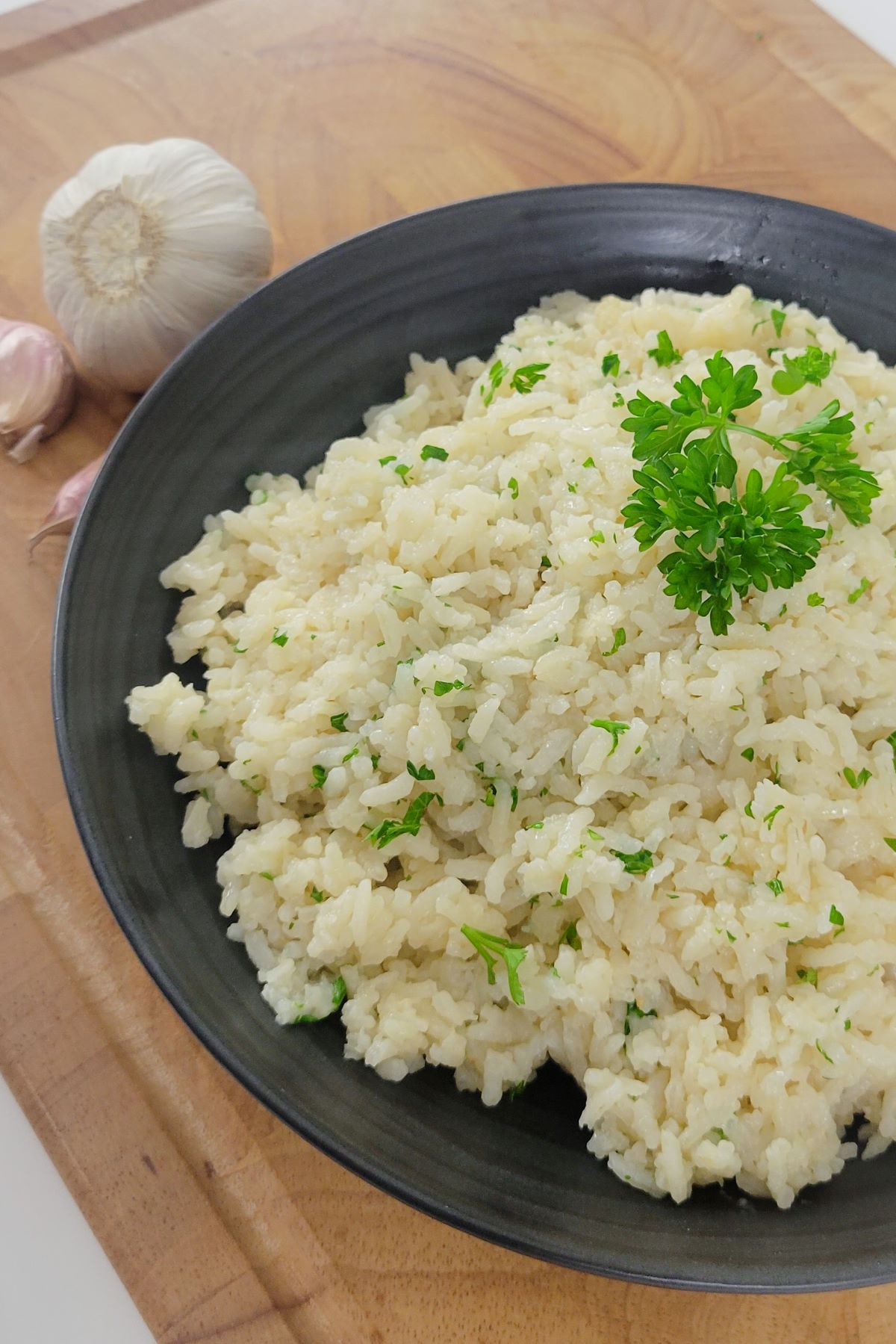 This is a close up image of buttered garlic rice in a black bowl. 