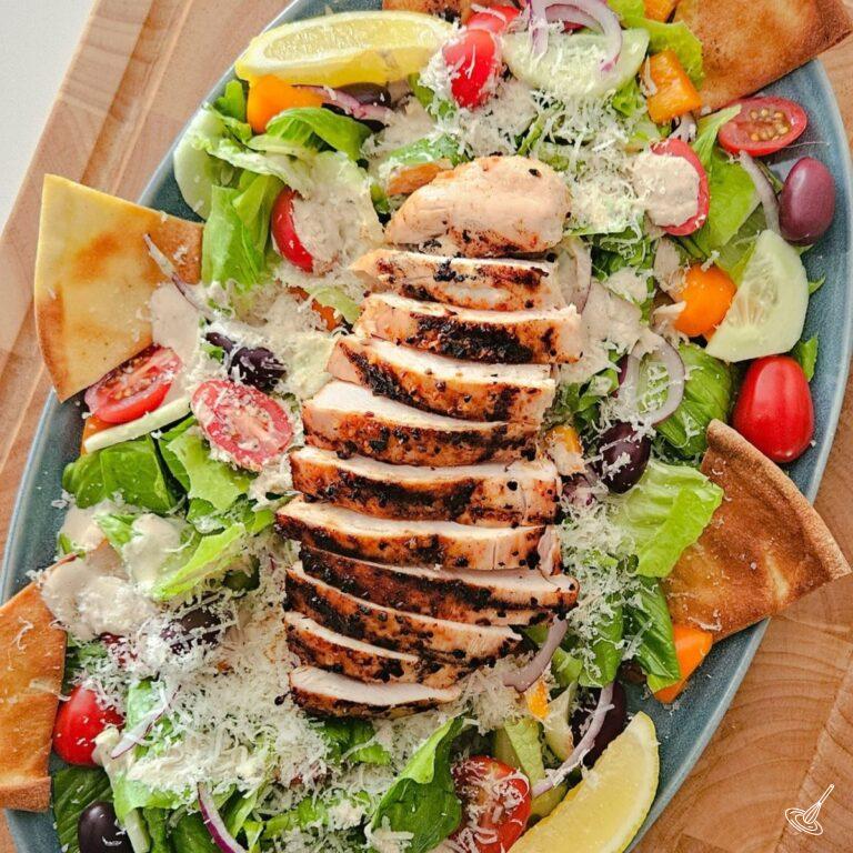 This is an image of a Greek Caesar Salad with a sliced bbq chicken on top.
