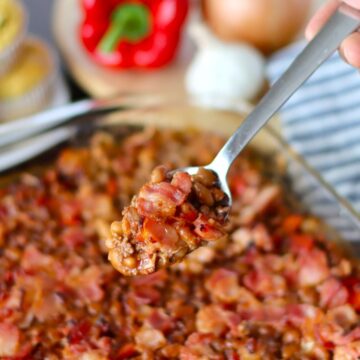 Someone taking a spoonful of baked beans with ground beef from the baking dish.