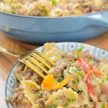 This is an image of a bowl of Philly Cheesesteak Pasta with a large pot of the same dish in the background.
