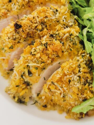 This is an image of a cooked and slice, breaded chicken breast, in a plate with salad.