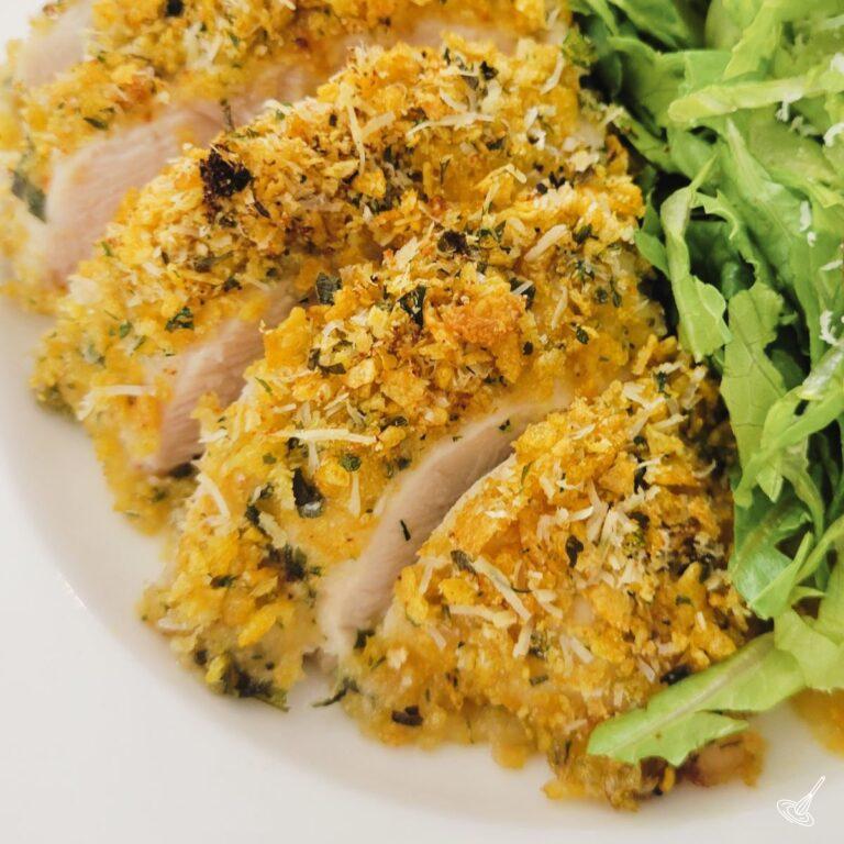 This is an image of a cooked and slice, breaded chicken breast, in a plate with salad.