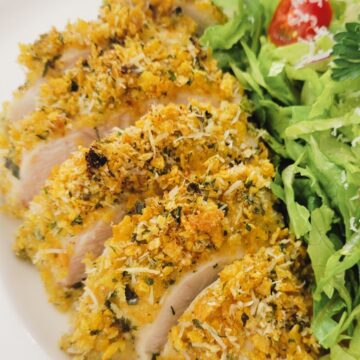 This is an image of a cooked and sliced, breaded chicken breast on a plate with a salad.