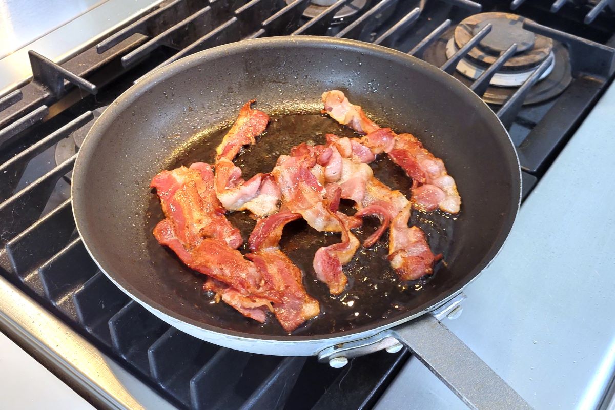 This is an image of a bacon cooking in a frying pan on the stove. 