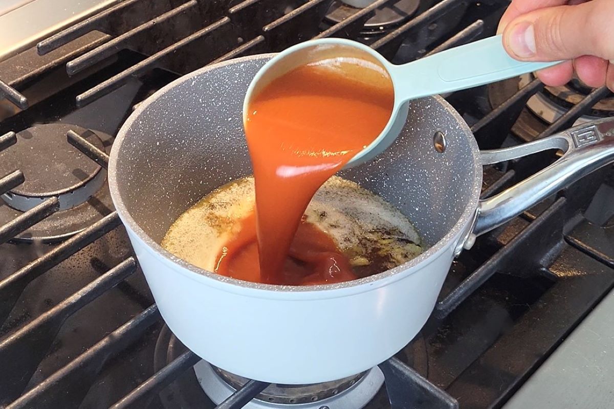 This is an image of someone pouring hot sauce in a saucepan which contains ingredients to make buffalo sauce. 