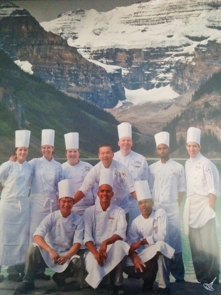 A group picture of chefs, standing in front of a lake with a mountain range.