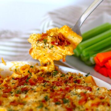 Spoon of Buffalo Chicken Mac and Cheese over its baking dish with chopped vegetables.