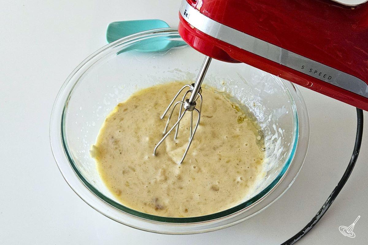 Someone using a hand blender to mix a batter inside of a mixing bowl.
