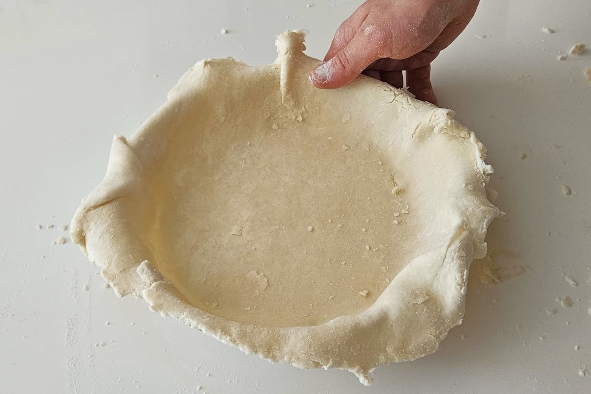Someone shaping dough in the bottom of a pie plate. 