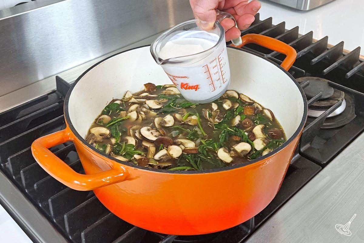 Someone pouring in heavy cream inside of a soup. 