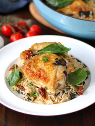 Baked chicken thigh on top of a bed of rice on a plate.