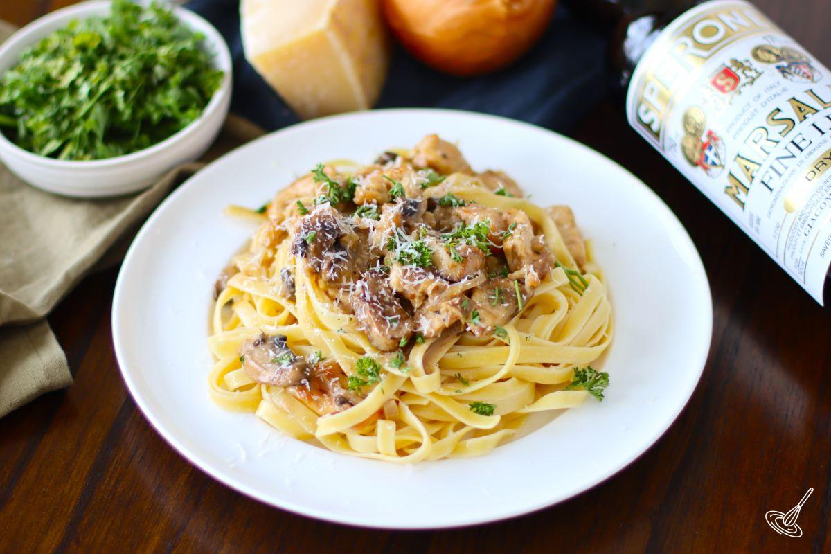 A plate of Chicken Marsala Fettuccine, topped with chopped parsley and freshly grated parmesan.
