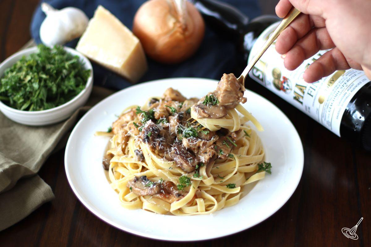 Someone holding a fork over a plate of chicken marsala fettuccine.