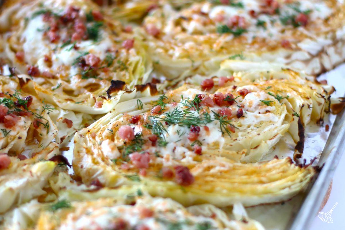 Slices of Cheesy Cabbage Steak on a baking sheet with fresh dill garnish.