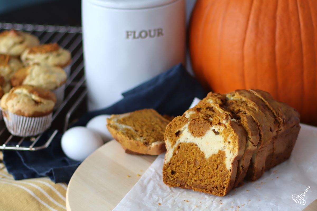 A sliced loaf of Pumpkin Swirl Bread with Pumpkin swirl muffins beside it.
