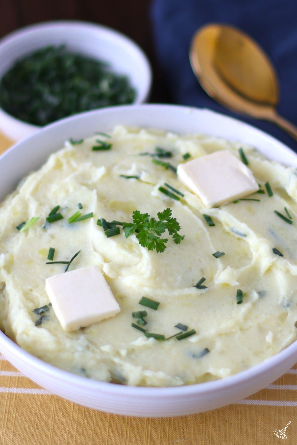 Cottage Cheese Mashed Potatoes in a bowl with pieces of butter and chives on top.