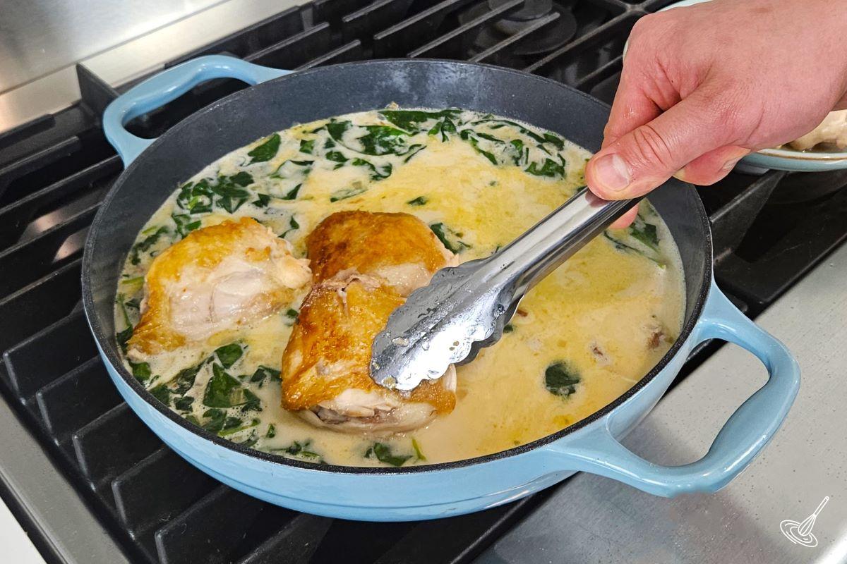 Someone placing chicken thighs in a skillet which contains rice, broth, and veggies.