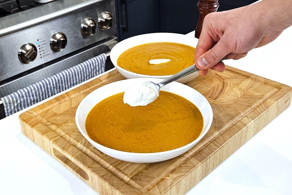 Someone placing a dollop of sour cream on top of a bowl of Tomato Fennel Soup. 