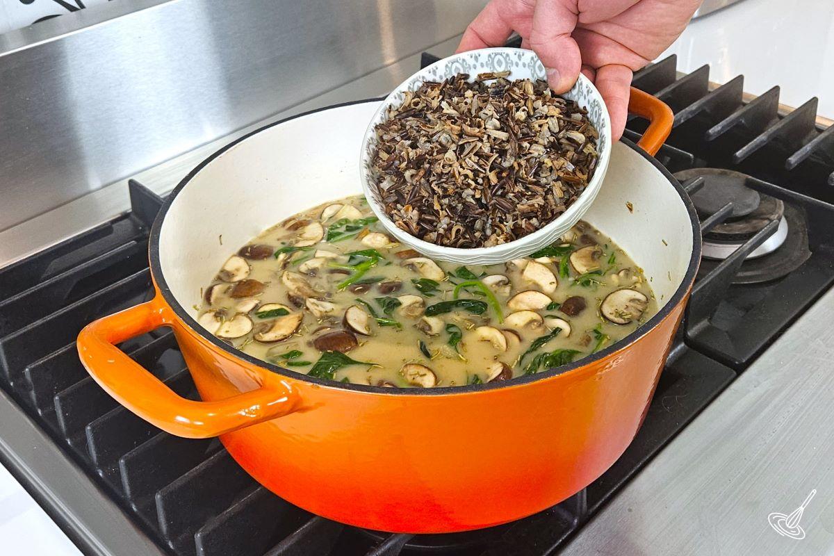 Someone placing cooked wild rice in a vegetable soup. 
