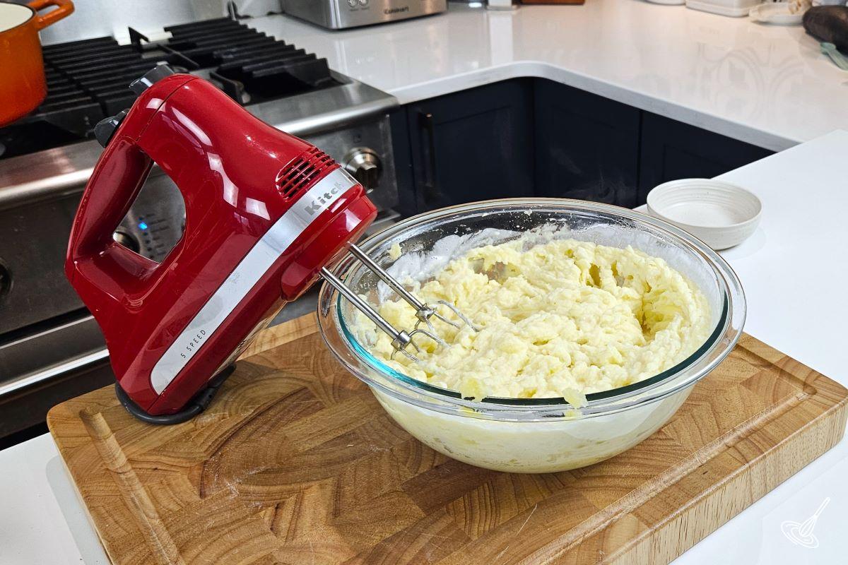 Someone using a hand blender to make a bowl of mashed potatoes.