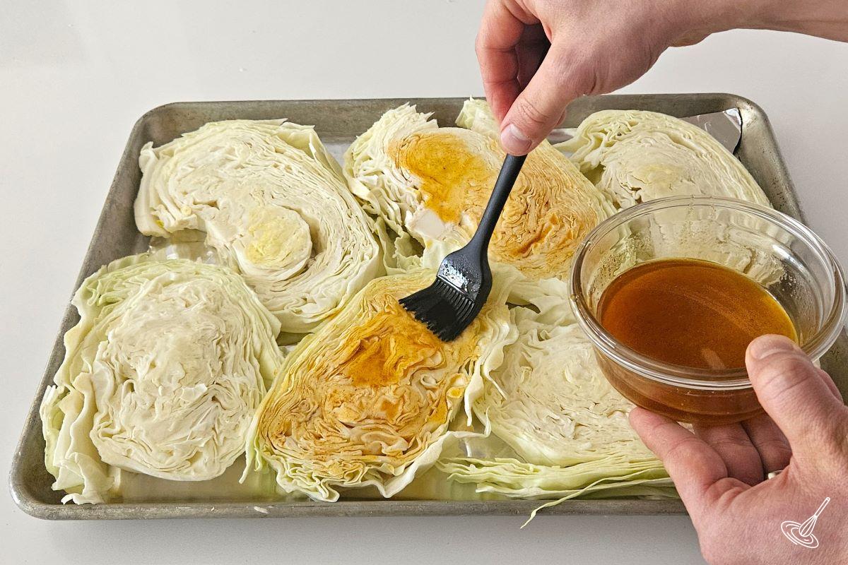 Someone brushing an olive oil mixture on top of slices of cabbage on a tray.