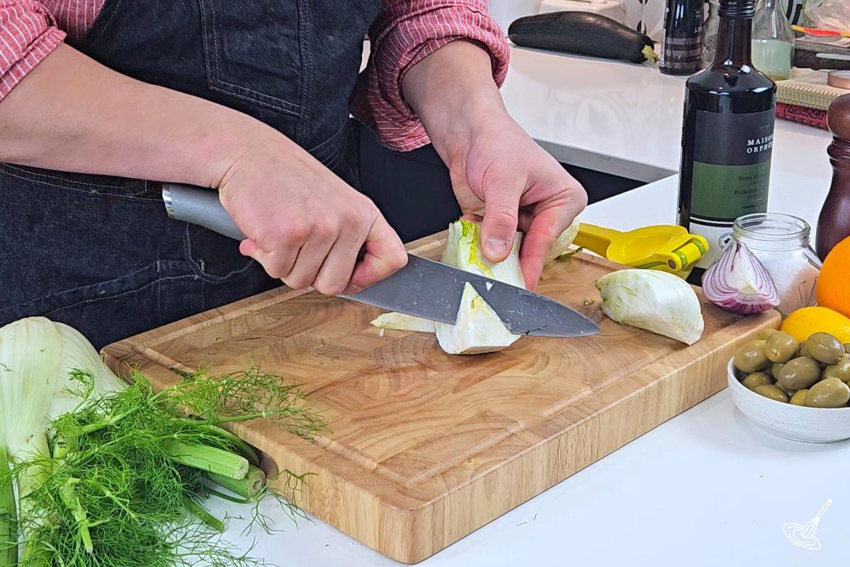 Someone cutting off the core of the fennel bulb piece. 