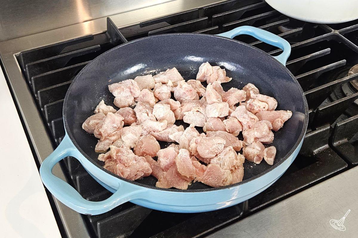 Cubed of chicken cooking in a large skillet.