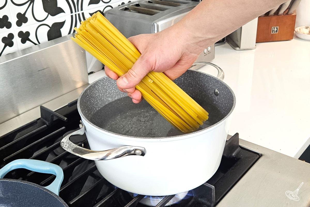 Someone placing a handful of pasta into a large pot of boiling water.