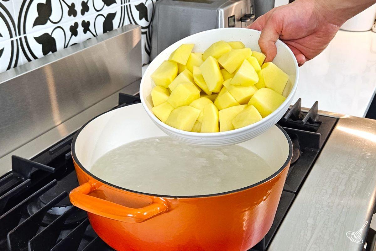 Someone placing chopped potatoes into a pot of boiling water.