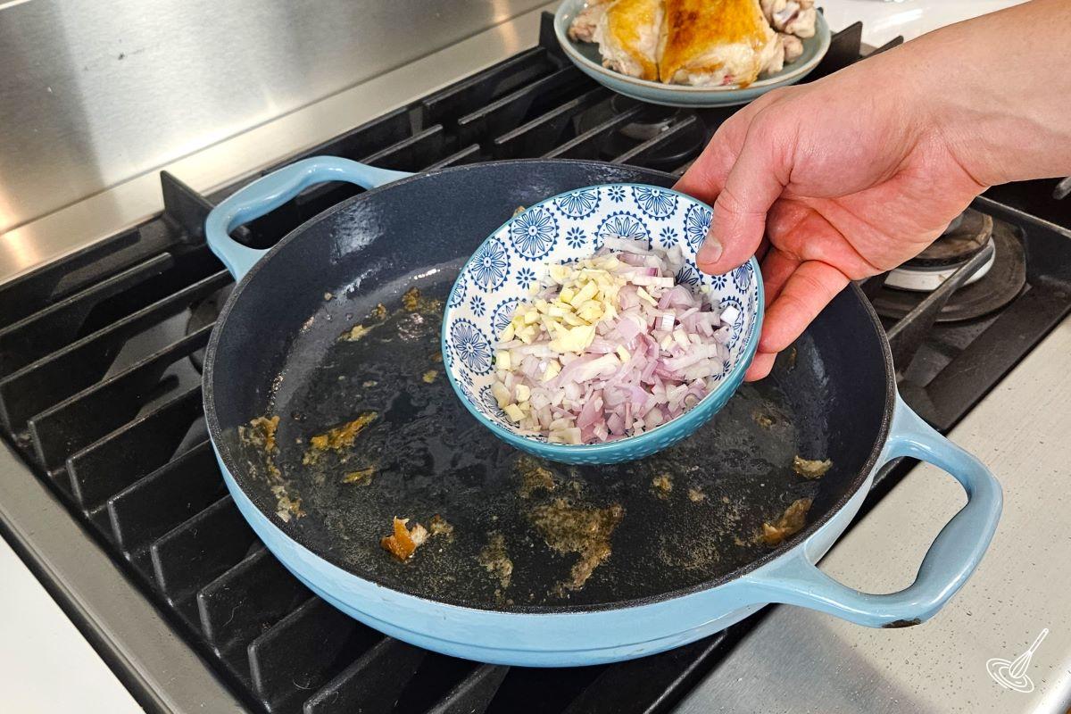 Someone placing chopped shallots and garlic in a skillet to cook.