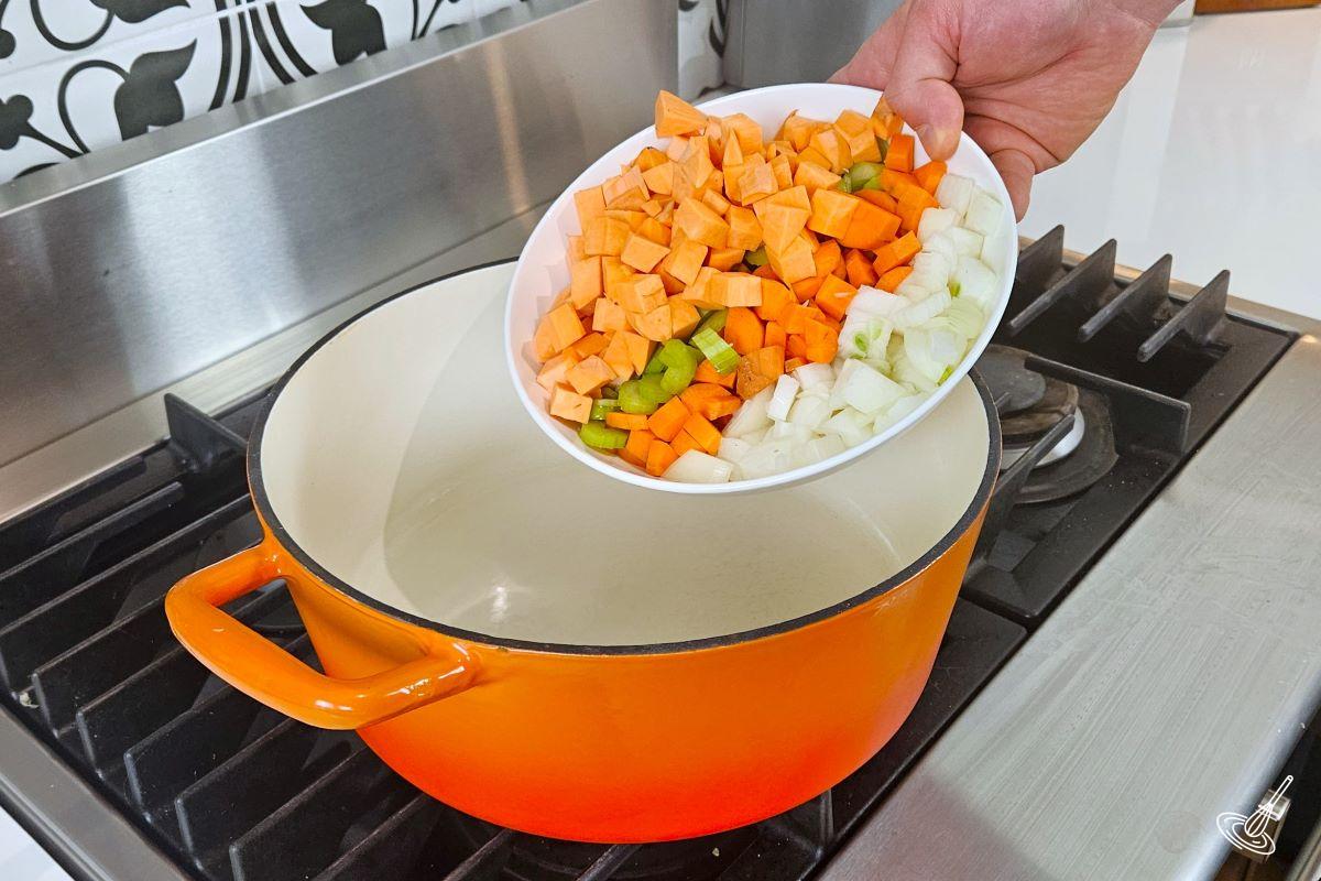 Someone placing chopped vegetables in a large Dutch oven. 