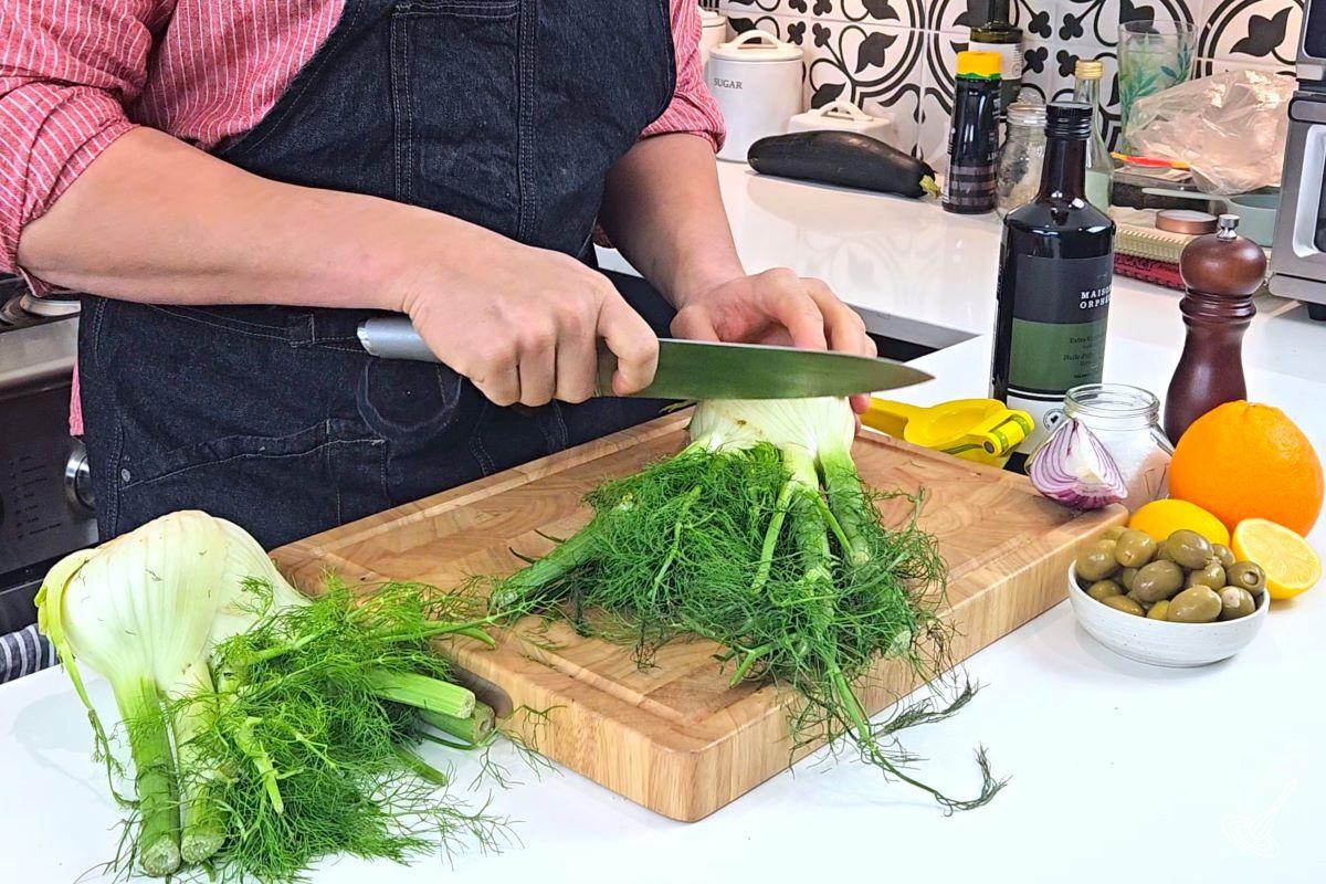 Someone cutting the stalks off of a bulb of fennel.