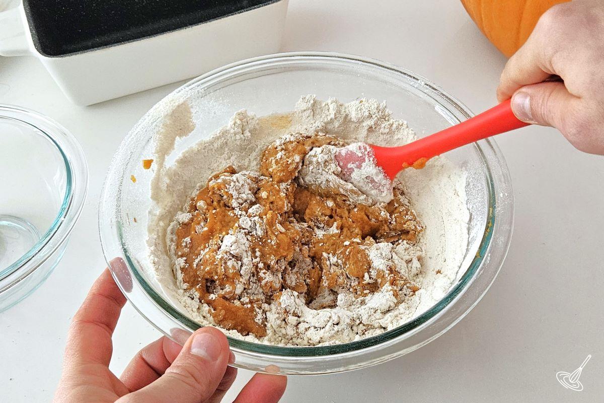 Someone folding wet and dry ingredients together to make a pumpkin cake batter.