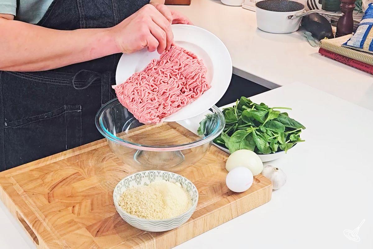 Someone placing ground turkey into a large mixing bowl with panko crumbs and parmesan. 