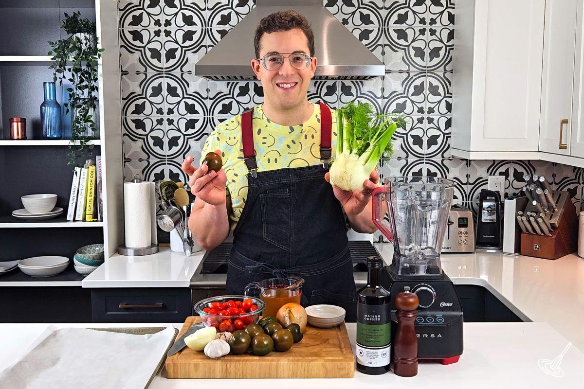 Someone standing in a kitchen and holding up a fennel and a tomato.