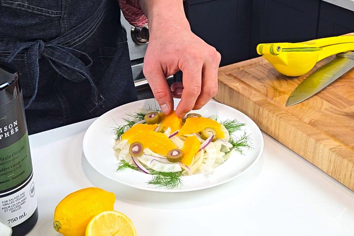 Someone assembling a Sicilian Salad on a plate. 