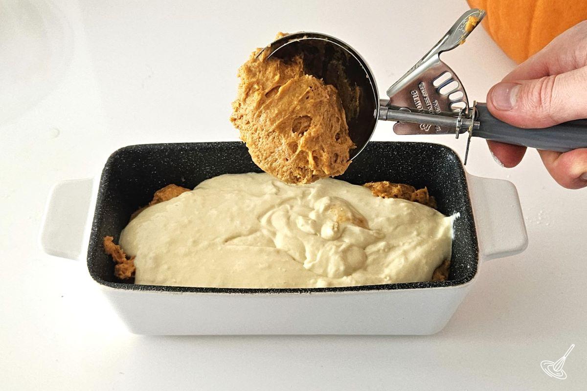 Someone scooping pumpkin cake batter into a half filled loaf pan.