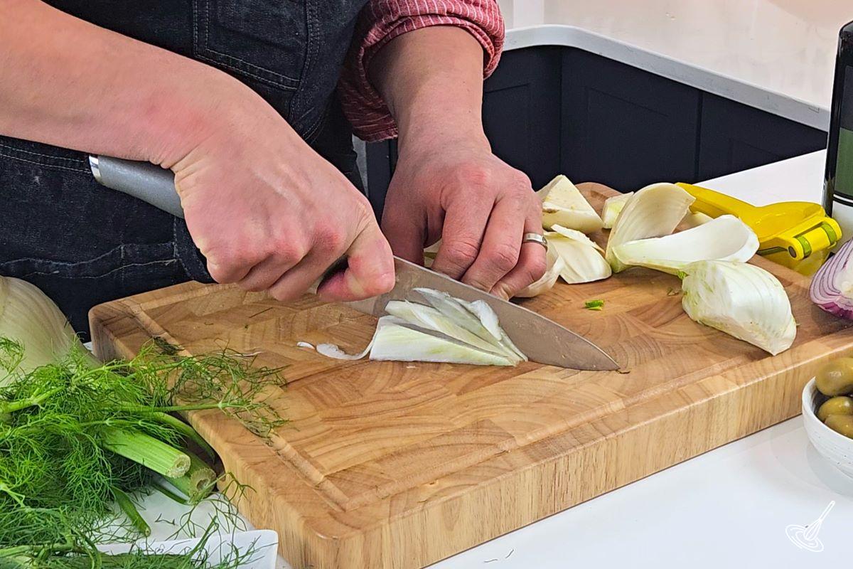 Someone thinly slicing pieces of fennel bulb.