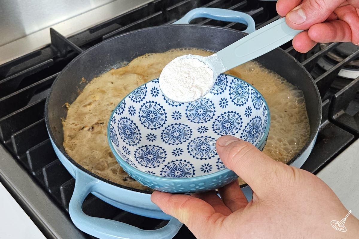 Someone placing a tablespoon of flour in a small bowl.