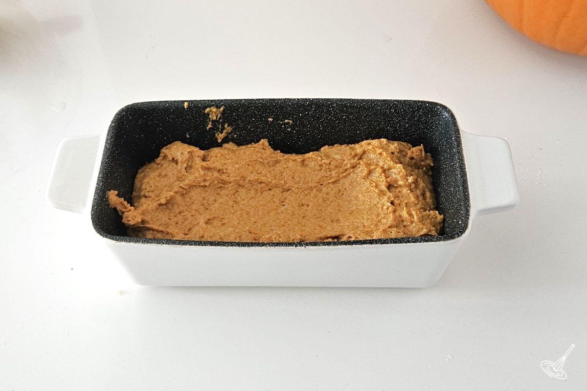 A loaf pan, half filled with pumpkin cake batter.