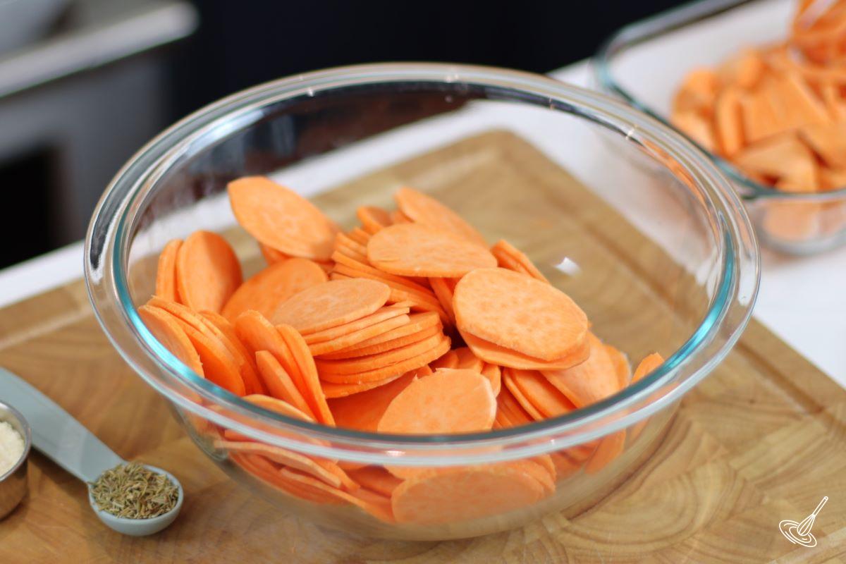 Slices of sweet potato in a large bowl with melted butter. 