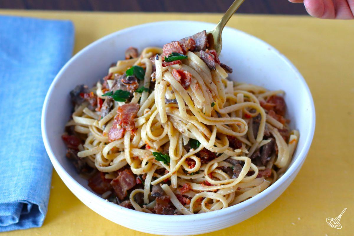 Someone take a fork full of pasta with bacon.