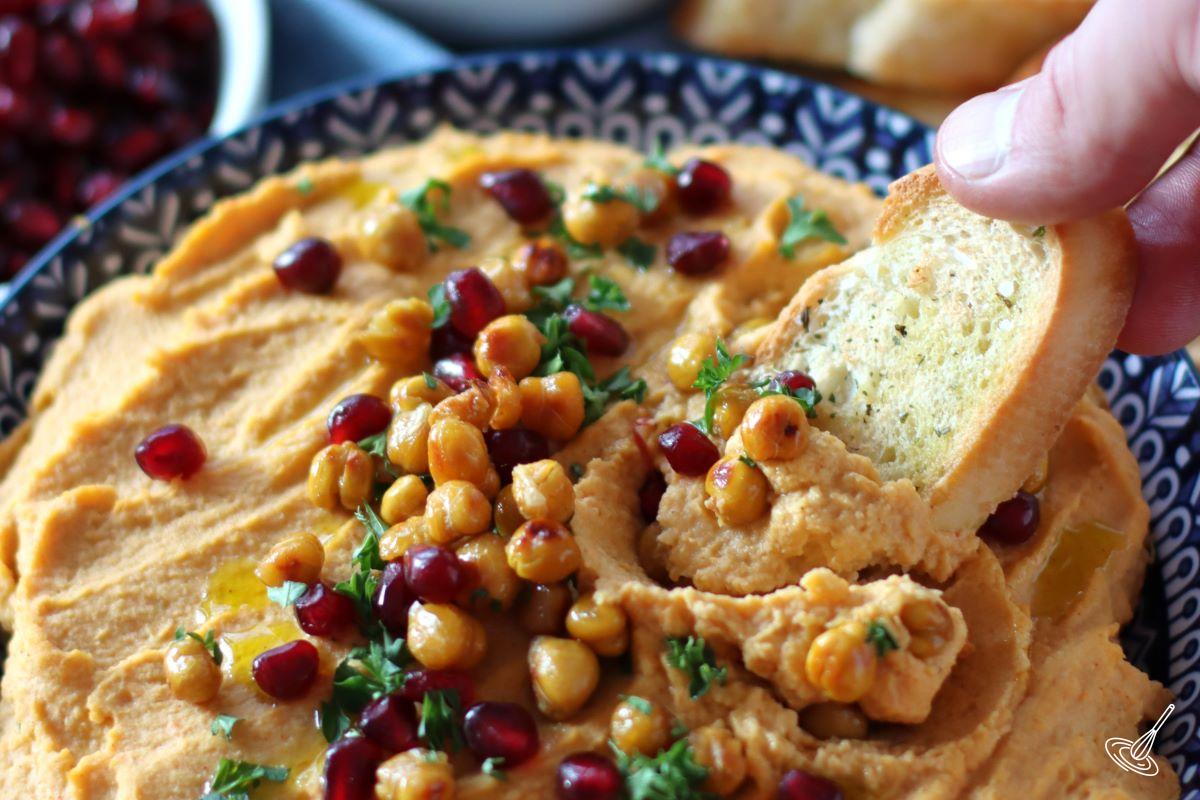 Someone scooping up hummus with a crostini. 