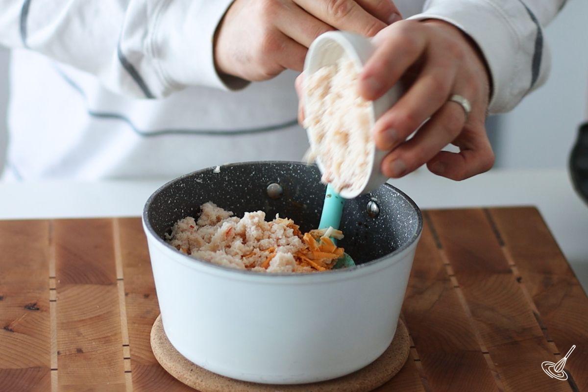 Someone adding crab meat to a crab puffs filling.