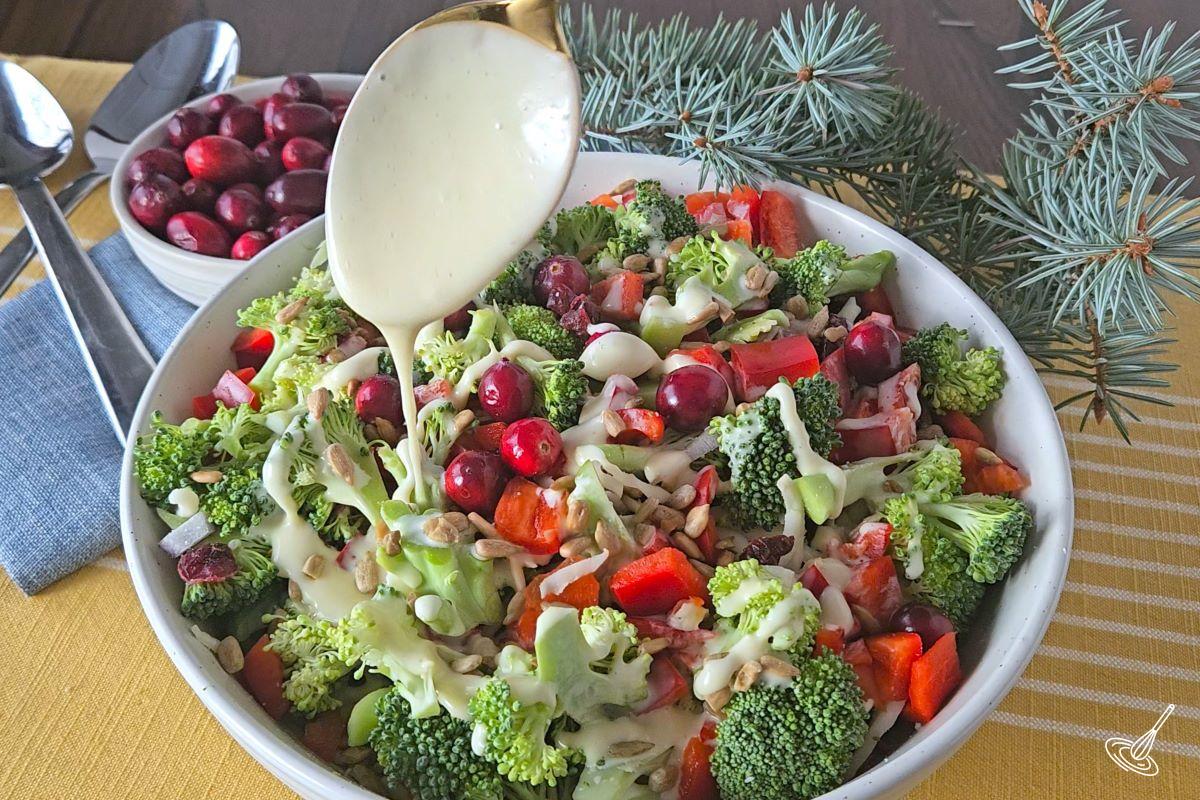 Someone pouring salad dressing over the Broccoli Salad with Cranberries and sunflower seeds. 