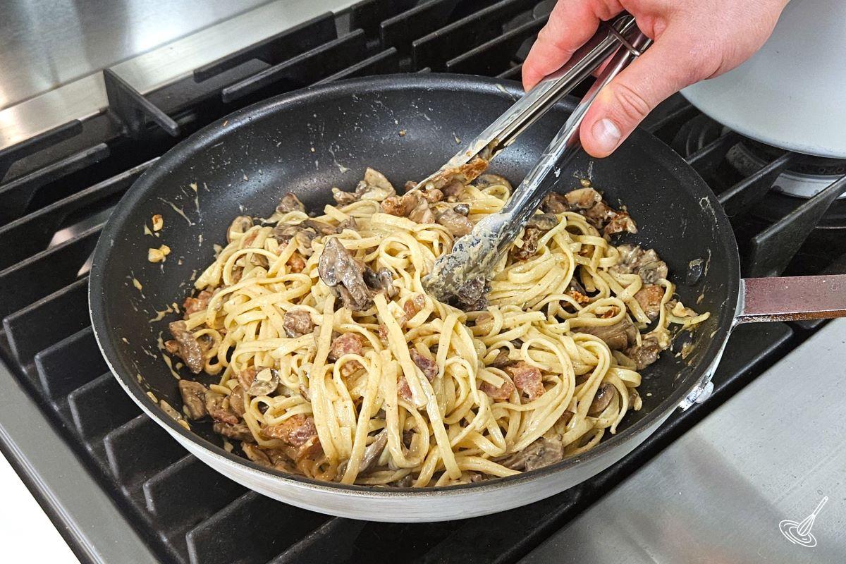 Pasta being tossed in a mushroom and bacon sauce. 