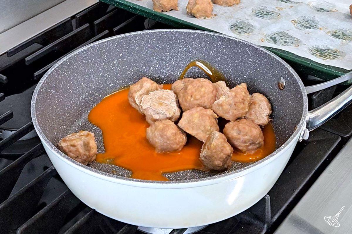 Meatballs and buffalo sauce in a skillet.