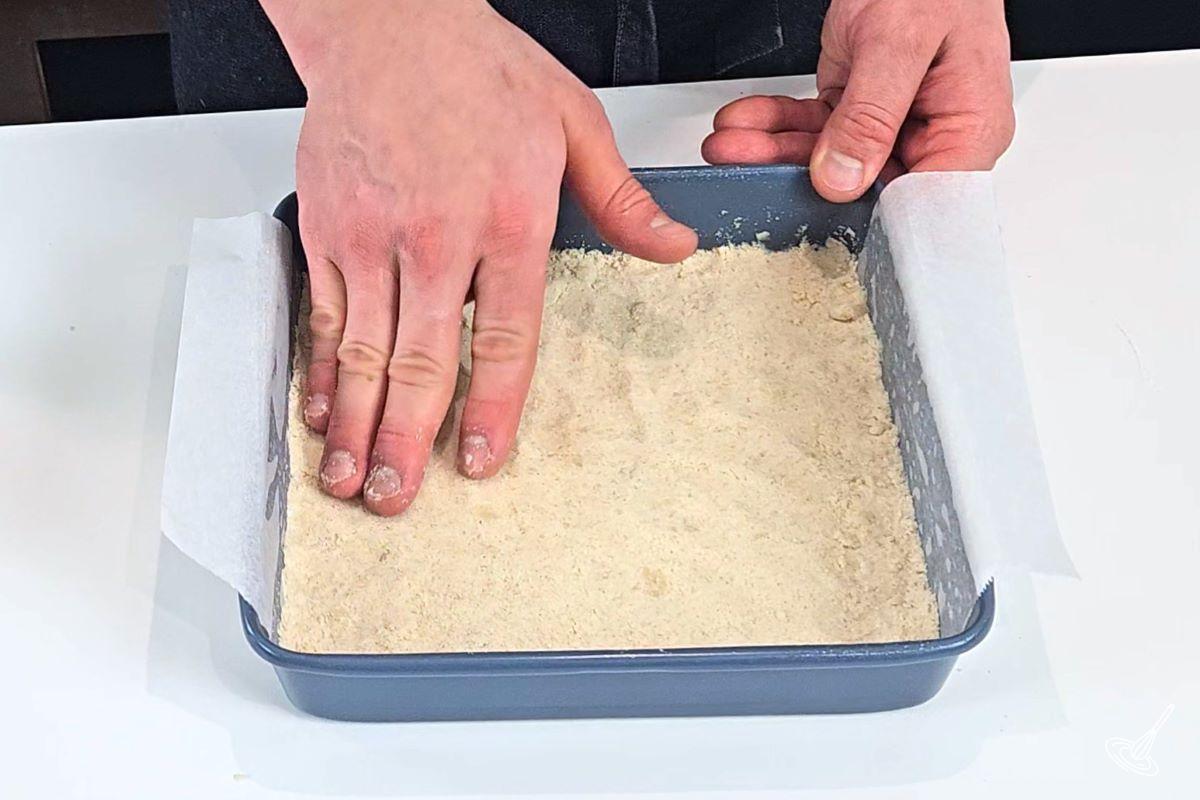 Someone using their hand to press down on dough inside of a pan.
